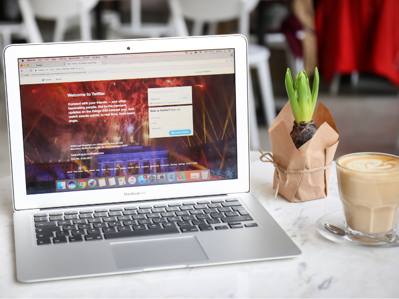 Fotografía de un portátil sobre la mesa de una cafetería, en cuya pantalla se ve la página web inicial de Twitter.
