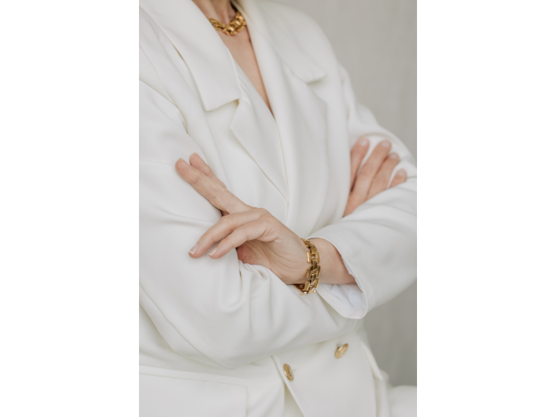 Fotografía de un conjunto de chaqueta blanca y bisutería dorada puestas en una persona, ejemplo de buena etiqueta para el marketing en Marbella